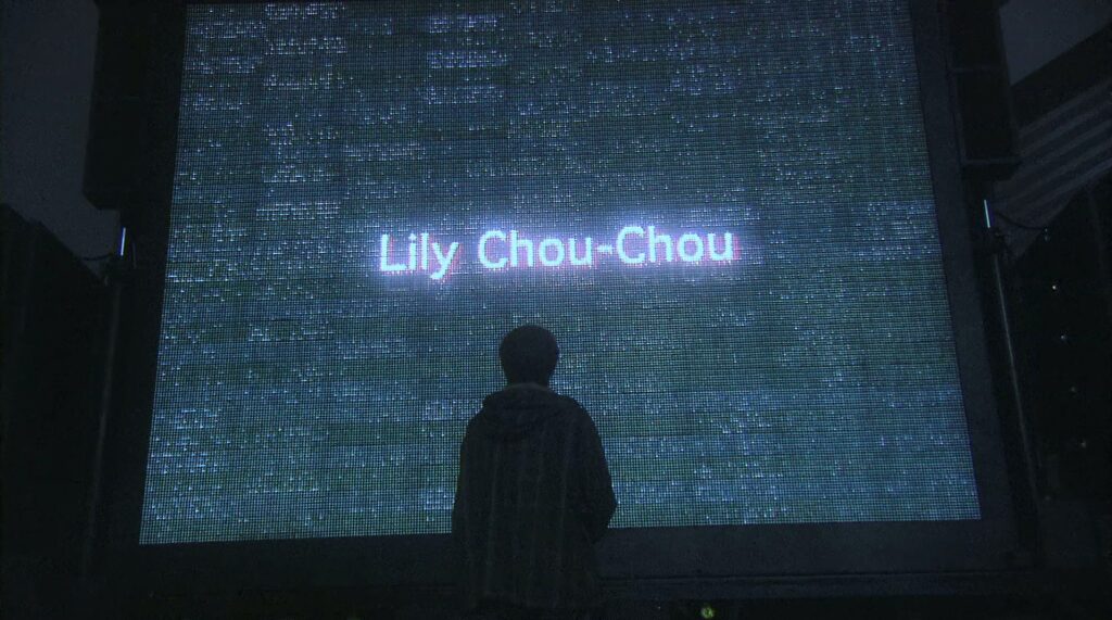 Music becomes an escape in All About Lily Chou-Chou (2001) as a student gazes at a screen bearing Lily Chou-Chou's name.