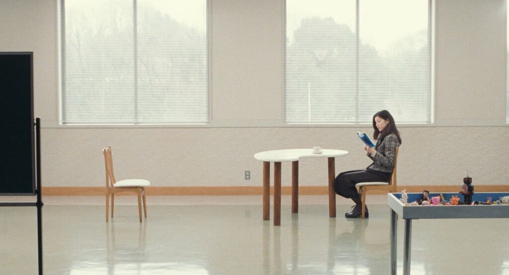 A woman sits alone reading in a sparse room in Cure (1997).