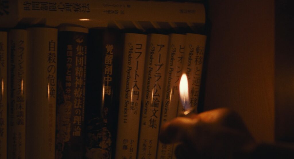 A hand holds a lighter near a row of books in Cure (1997).