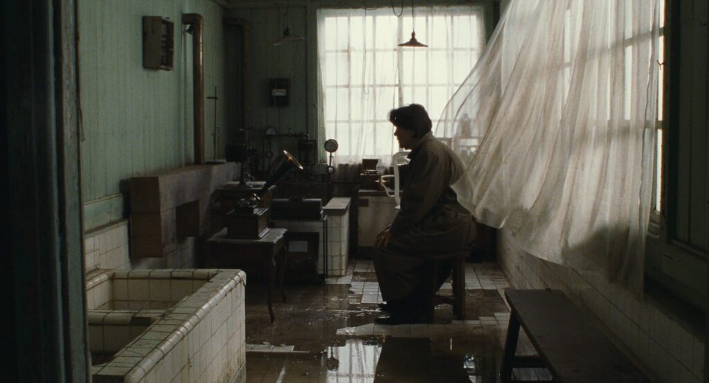 A solitary figure sits in a room with sunlight filtering through curtains in Cure (1997).