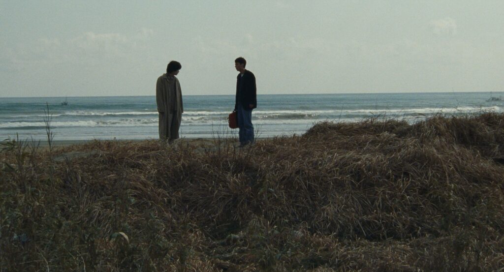 Two men stand overlooking the shoreline in Cure (1997).