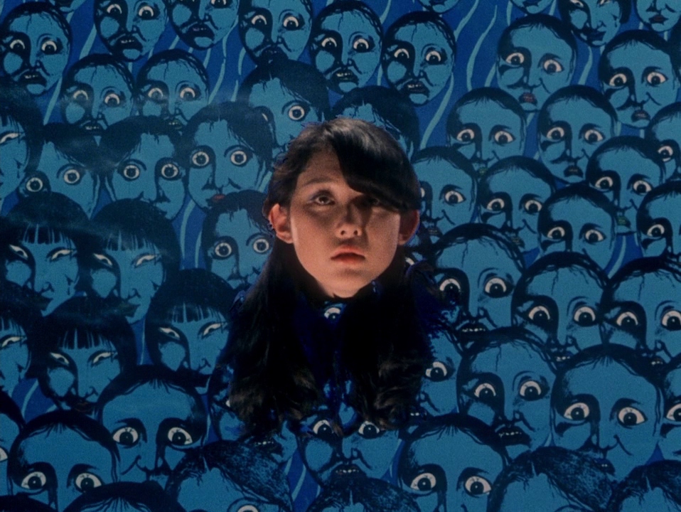 A close-up of a girl framed by a wall of illustrated faces in House (1977).