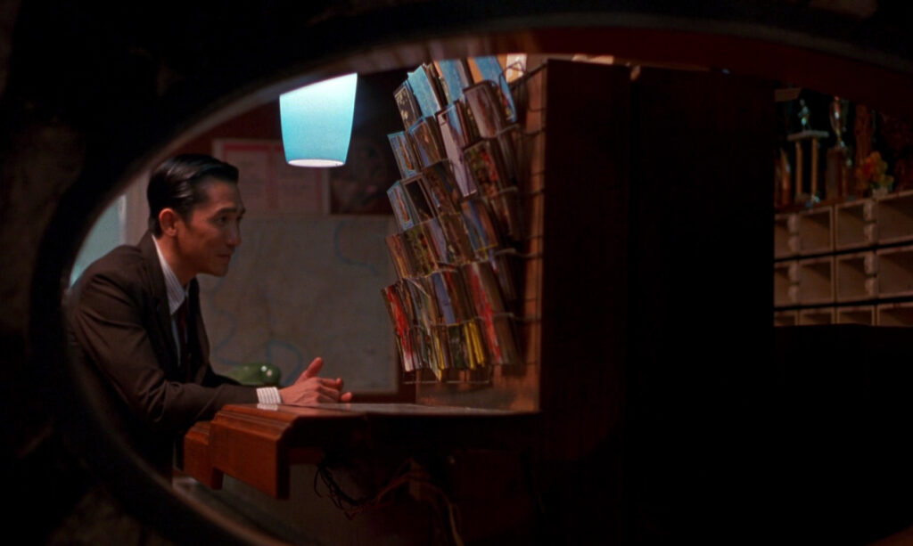 Tony Leung sits in a quiet hotel lobby in In the Mood for Love (2000), showcasing Wong Kar-wai's cinematic style.