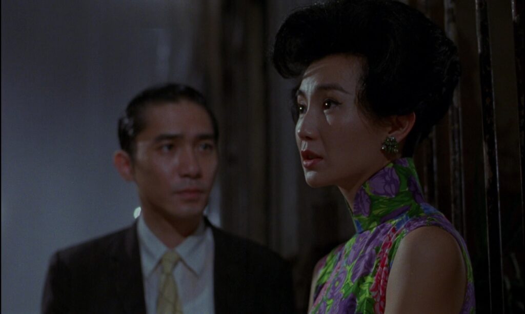 Maggie Cheung and Tony Leung share a tense moment in In the Mood for Love (2000), framed by elegant costume design and soft lighting.