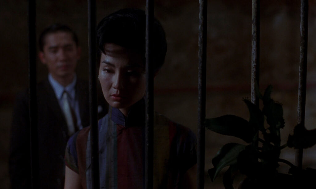 Maggie Cheung stands behind iron bars in In the Mood for Love (2000), emphasizing themes of longing and distance.