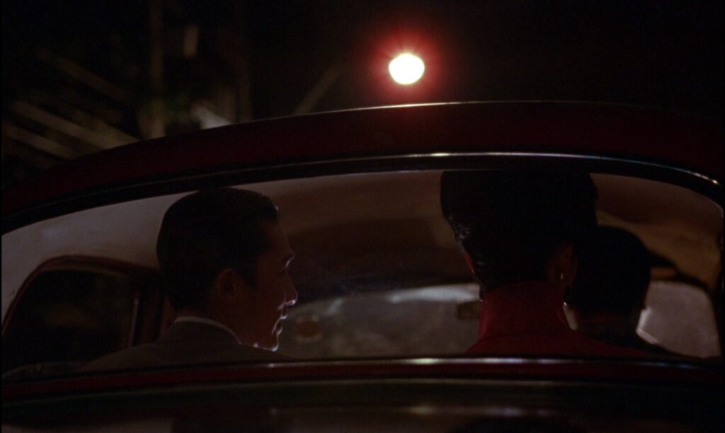 Tony Leung and Maggie Cheung sit together in a taxi at night in In the Mood for Love (2000), illuminated by warm city lights.