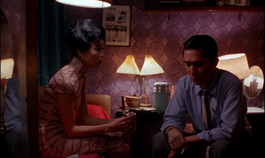 Maggie Cheung and Tony Leung share a contemplative moment in In the Mood for Love (2000), framed by warm interior lighting.