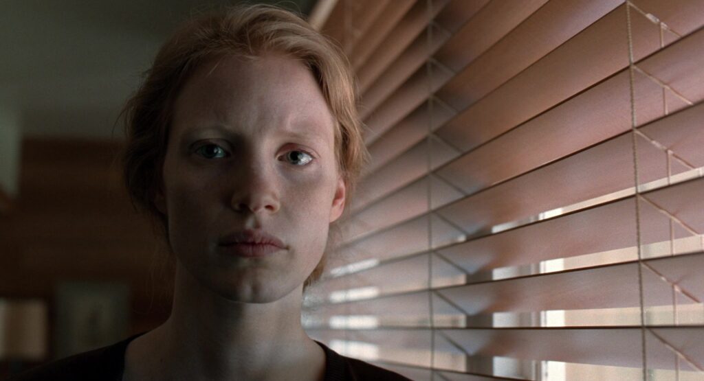 Jessica Chastain stands by a window in The Tree of Life (2011), illuminated by soft natural light.