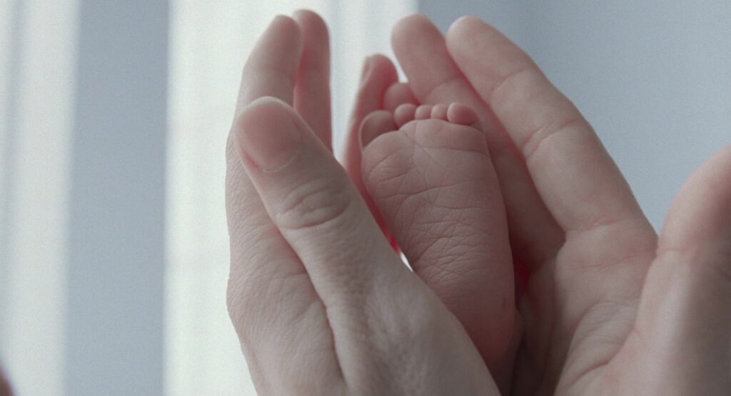 A newborn baby's feet held gently in caring hands in The Tree of Life (2011).
