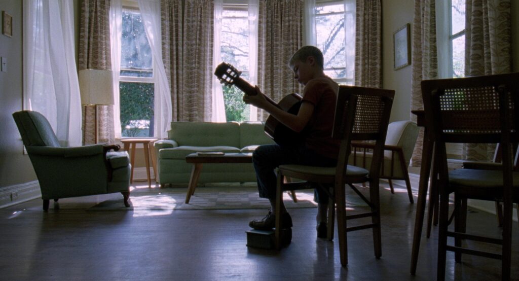 A young boy plays guitar in a sunlit living room in The Tree of Life (2011).