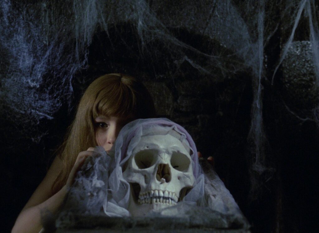 Valerie sits beside a skull draped with white fabric in Valerie and Her Week of Wonders (1970).