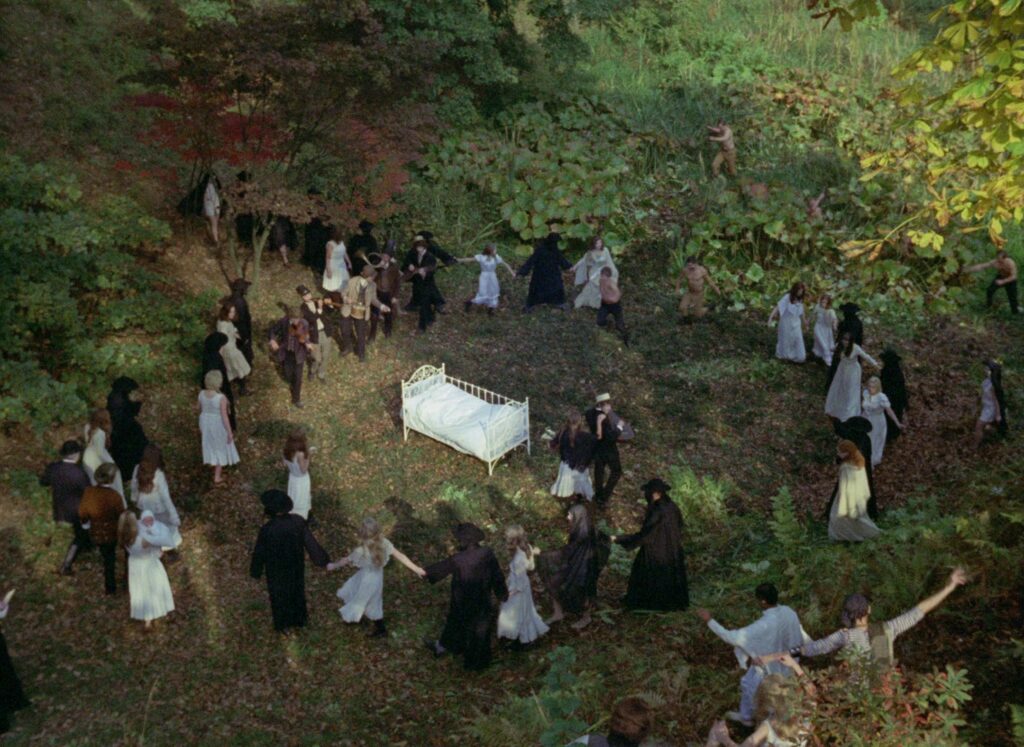 A gathering surrounds a white bed in a forest in Valerie and Her Week of Wonders (1970).