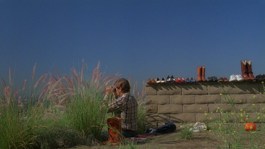 Travis Henderson sits alone beside a wall lined with shoes in Paris, Texas (1984), reflecting on his past.