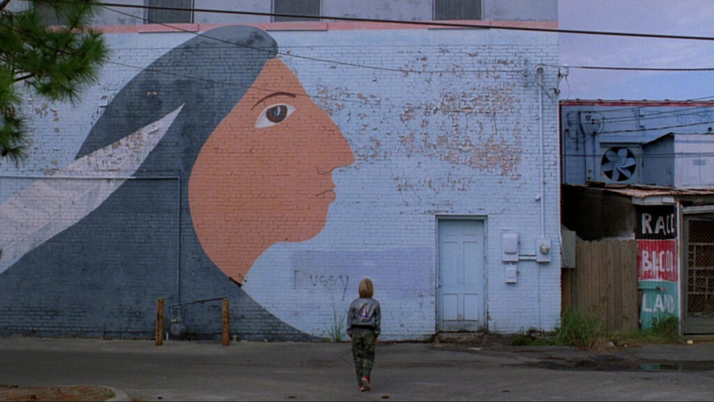 A lone figure stands before a large mural in Paris, Texas (1984), emphasizing themes of memory and identity.
