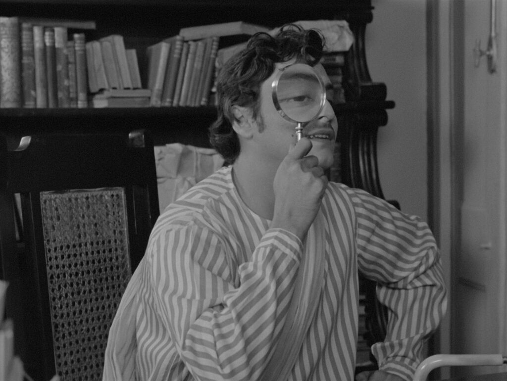 Amal peers through a magnifying glass with playful curiosity in Charulata (1964)