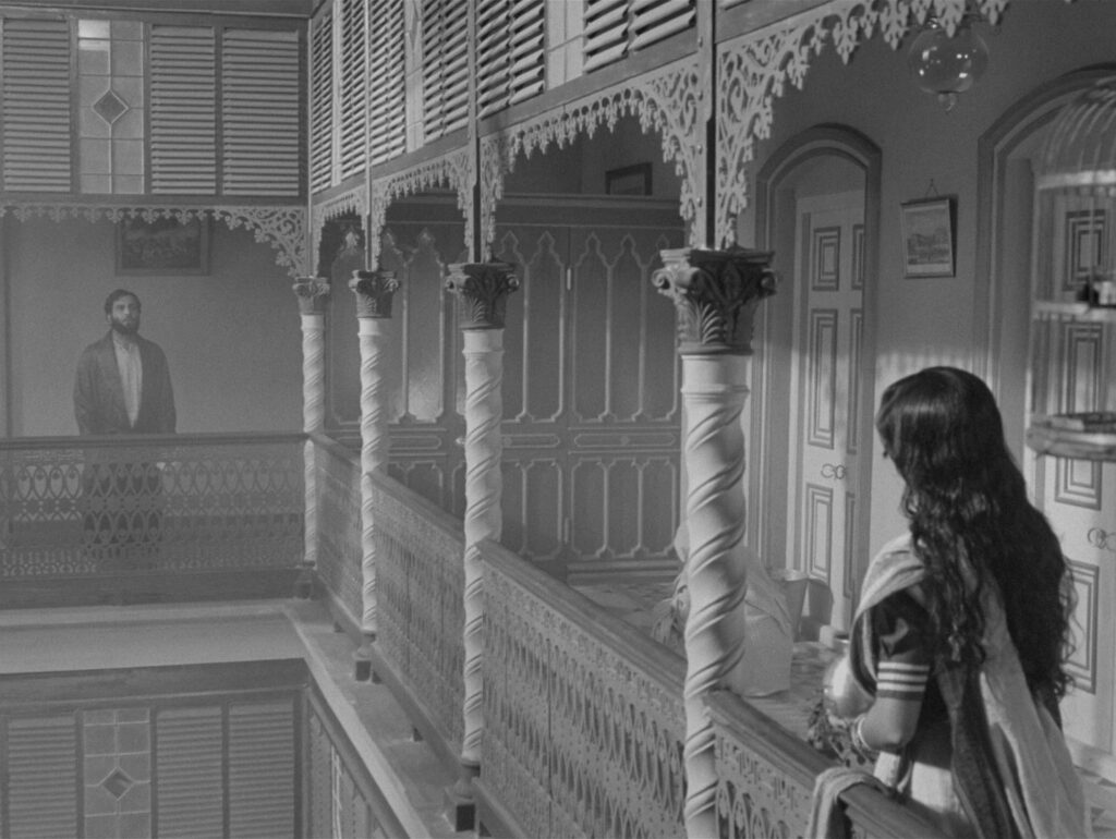 Charulata gazes across the balcony toward her husband's reflection in the distance, in Charulata (1964)