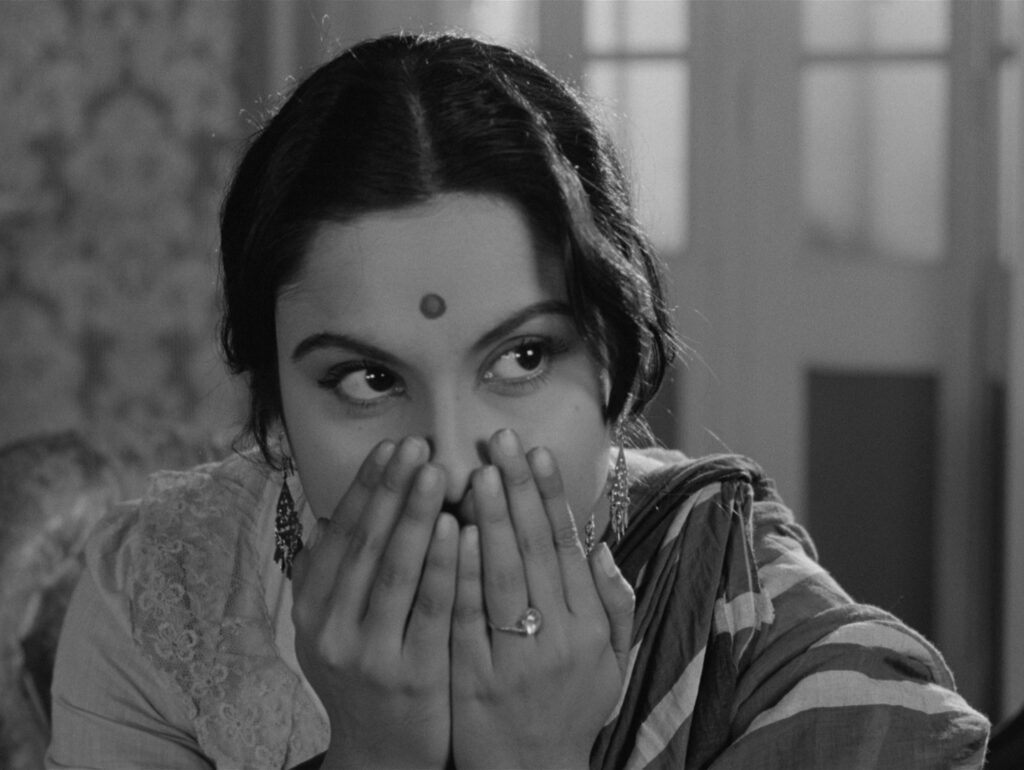 Charulata covers her mouth with both hands, blushing shyly, in Charulata (1964)