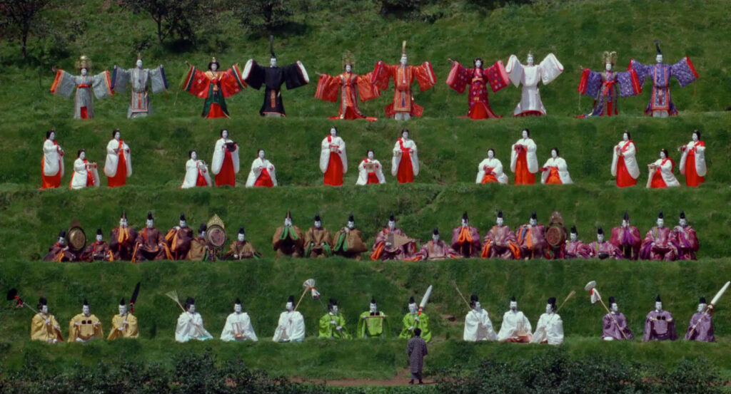 Rows of elaborately dressed ceremonial figures stand on a grassy hillside in Dreams (1990).