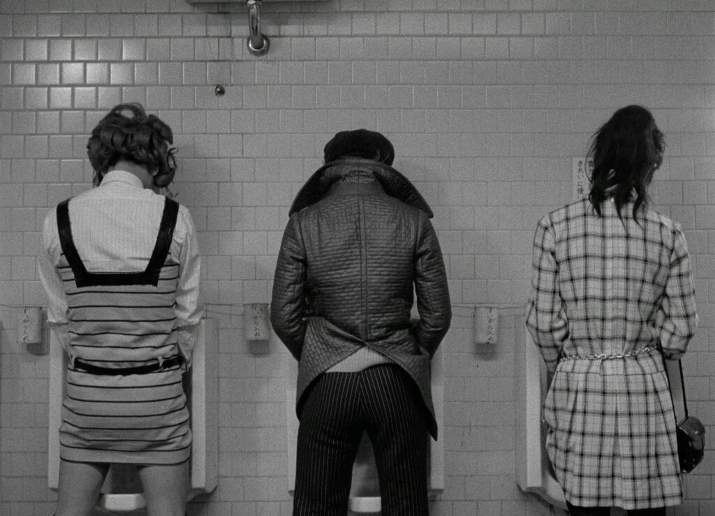 Three people stand side by side at urinals inside a public restroom in Funeral Parade of Roses (1969).