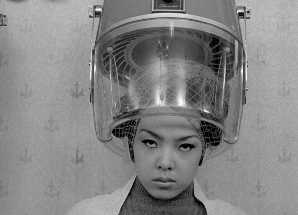 A young woman sits beneath a vintage salon hair dryer in Funeral Parade of Roses (1969).