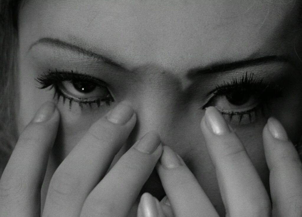A close-up of a young woman adjusting her eye makeup in Funeral Parade of Roses (1969).