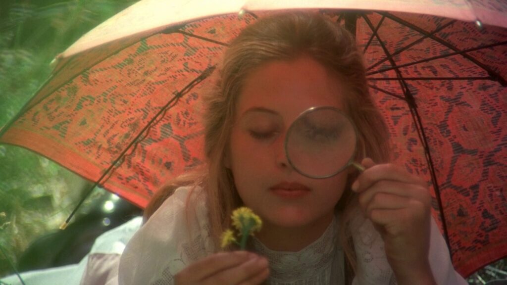 Miranda examines a flower through a magnifying glass under a lace parasol in Picnic at Hanging Rock (1975)