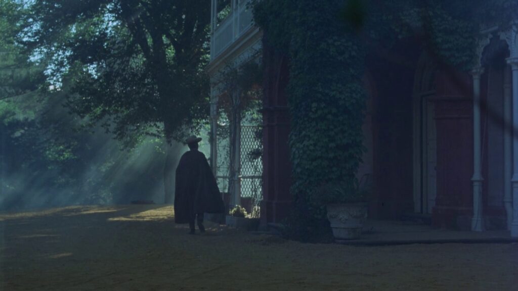 A cloaked figure walking past a colonial-era house at dusk in Picnic at Hanging Rock (1975)