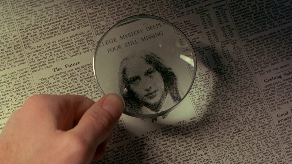 Newspaper clipping reading "College Mystery Deepens" viewed through a magnifying glass in Picnic at Hanging Rock (1975)