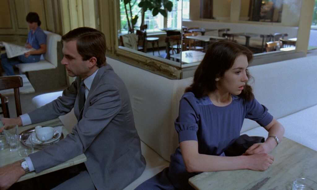 Sam Neill and Isabelle Adjani sitting back to back in a café scene from Possession 1981