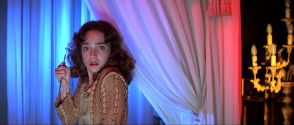 A frightened young woman stands beside colorful curtains in Suspiria (1977).