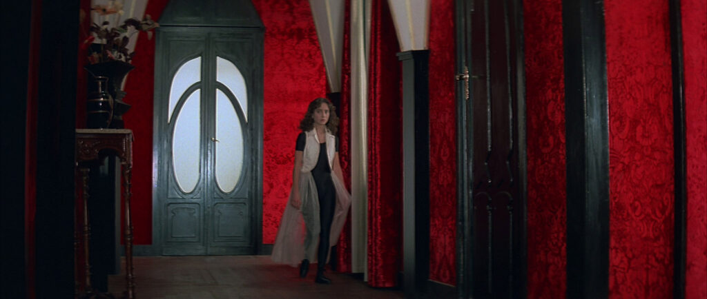 A young woman walks down a red hallway inside the academy in Suspiria (1977).