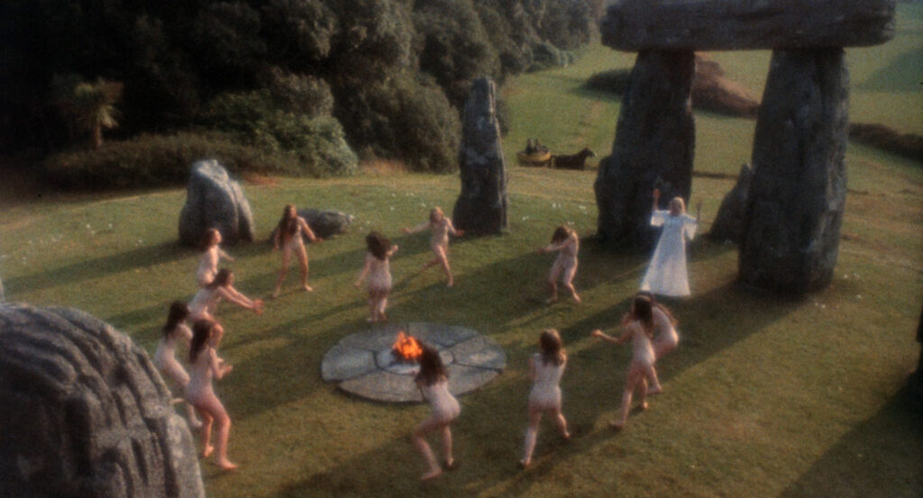 A group performs a ritual dance around a fire beside standing stones in The Wicker Man (1973).