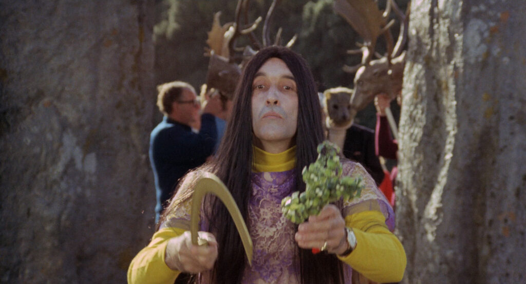 A ceremonial figure holds a sickle and greenery during a pagan ritual in The Wicker Man (1973).