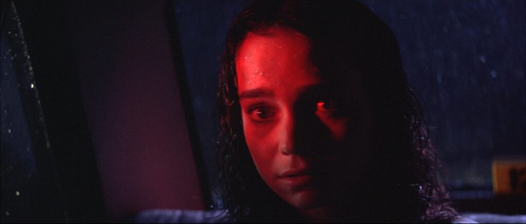 A frightened young woman illuminated by red light inside a car in Suspiria (1977).