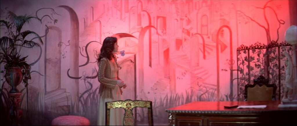 A woman stands inside a vividly painted room with surreal wall murals in Suspiria (1977).